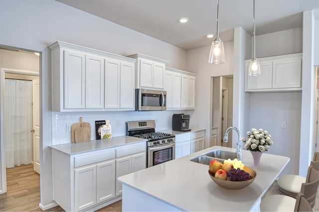 kitchen featuring sink, stainless steel appliances, light hardwood / wood-style floors, white cabinets, and decorative light fixtures