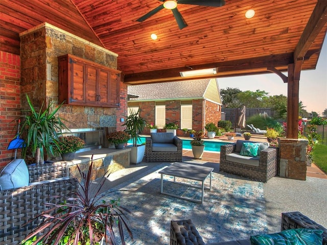 patio terrace at dusk featuring a fenced in pool, ceiling fan, and an outdoor stone fireplace