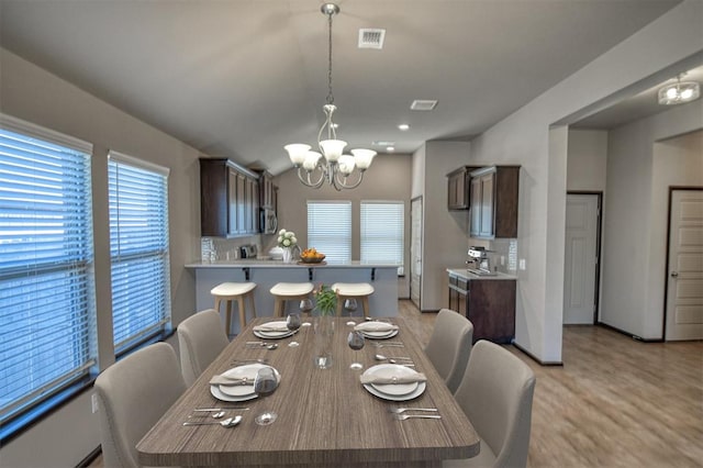 dining space featuring light wood-type flooring, vaulted ceiling, visible vents, and a notable chandelier