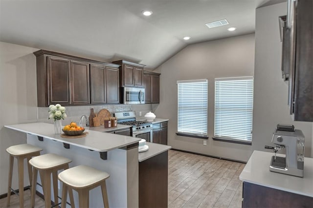 kitchen featuring a breakfast bar, lofted ceiling, light countertops, visible vents, and appliances with stainless steel finishes