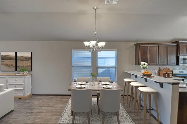 dining area featuring visible vents, baseboards, vaulted ceiling, light wood-type flooring, and an inviting chandelier