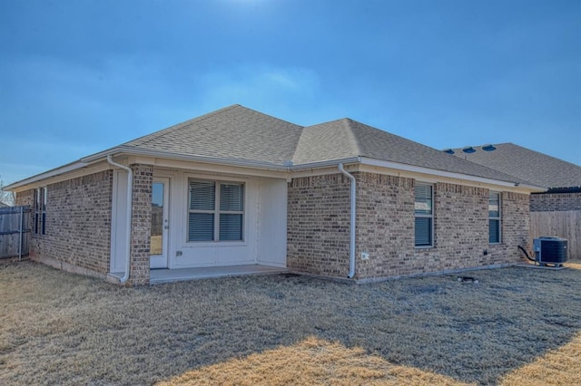 view of side of property with a shingled roof, cooling unit, brick siding, and fence