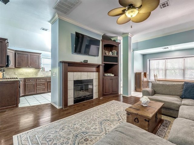 living room with crown molding, ceiling fan, a tiled fireplace, and light hardwood / wood-style floors