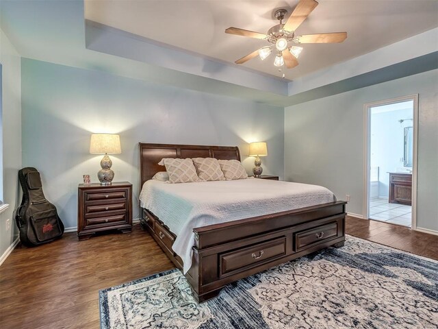 1801 Del Simmons Dr, Edmond, OK 73003 - bedroom with wood finished floors, a tray ceiling, connected bathroom, and ceiling fan
