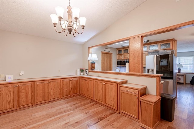 kitchen featuring kitchen peninsula, appliances with stainless steel finishes, pendant lighting, an inviting chandelier, and light hardwood / wood-style floors