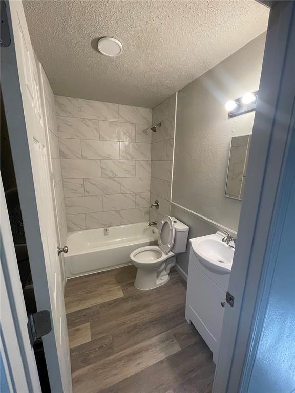 full bathroom with vanity, a textured ceiling, wood-type flooring, toilet, and tiled shower / bath