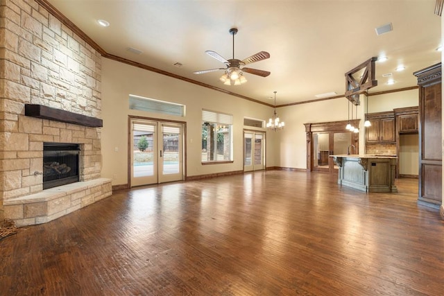 unfurnished living room featuring dark wood-type flooring, french doors, ornamental molding, a fireplace, and ceiling fan with notable chandelier