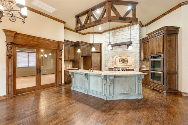 kitchen featuring sink, double oven, light stone counters, a center island with sink, and decorative light fixtures