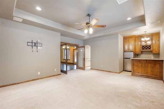 unfurnished living room with ceiling fan with notable chandelier, light carpet, and a tray ceiling