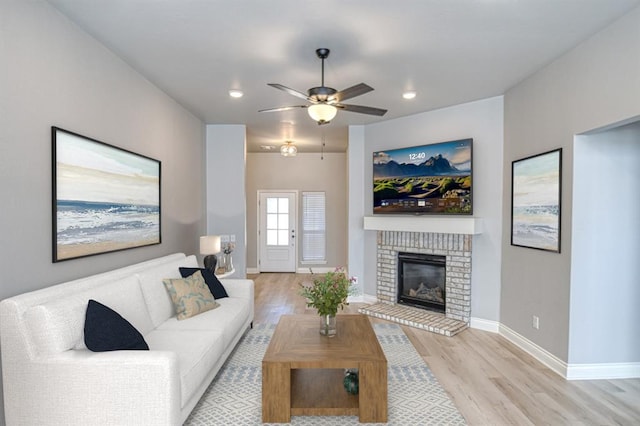 living room featuring a fireplace, ceiling fan, and light wood-type flooring