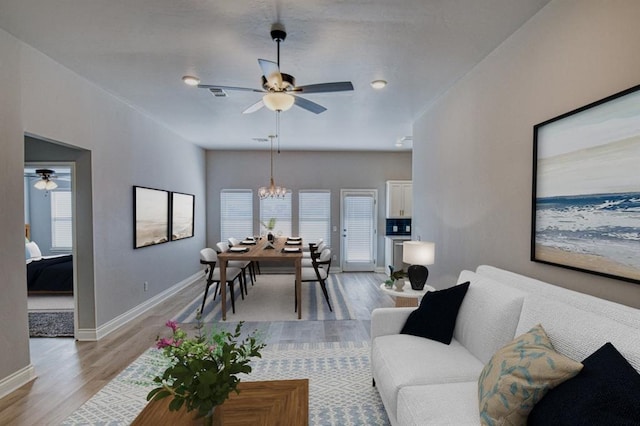 living room featuring ceiling fan with notable chandelier and light hardwood / wood-style flooring