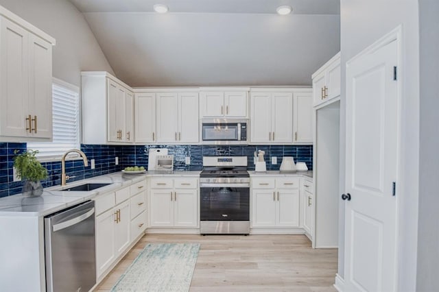 kitchen featuring stainless steel appliances, vaulted ceiling, sink, and white cabinets