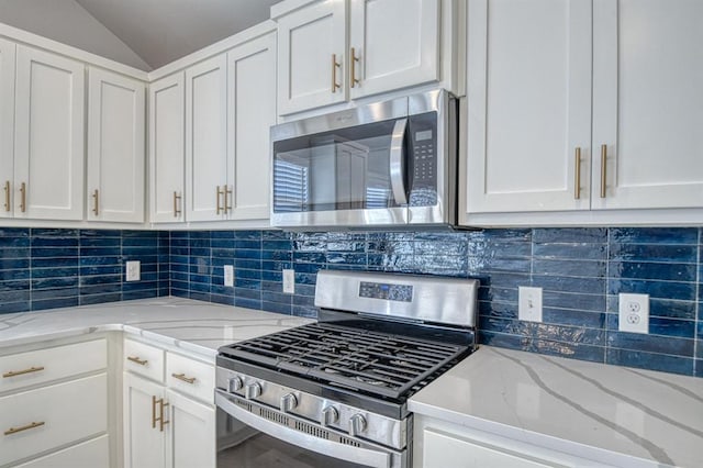 kitchen with lofted ceiling, appliances with stainless steel finishes, backsplash, light stone counters, and white cabinets