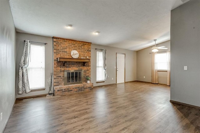 unfurnished living room featuring a brick fireplace, plenty of natural light, wood-type flooring, and vaulted ceiling