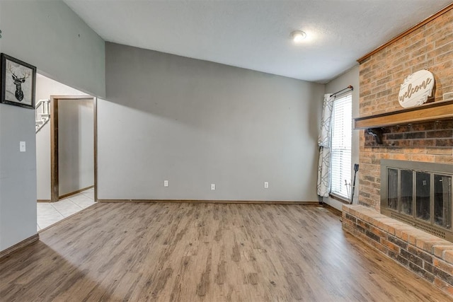 unfurnished living room with light wood-type flooring, a textured ceiling, and a brick fireplace