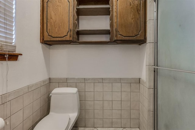 bathroom with toilet, tile walls, and a shower with shower door