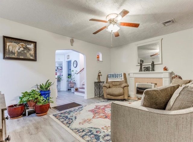 living room featuring a tiled fireplace, hardwood / wood-style flooring, ceiling fan, a textured ceiling, and heating unit