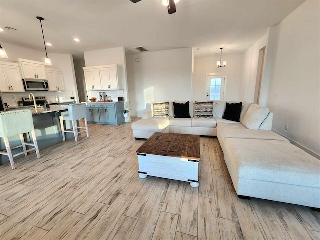 living room featuring ceiling fan with notable chandelier, light wood-type flooring, and sink