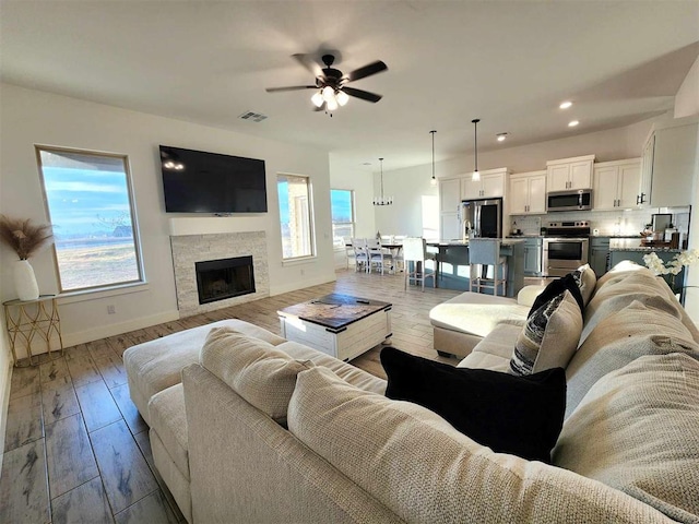 living room featuring ceiling fan, a stone fireplace, and light hardwood / wood-style flooring