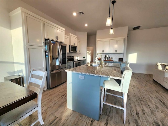 kitchen featuring backsplash, stainless steel appliances, stone countertops, white cabinetry, and hanging light fixtures