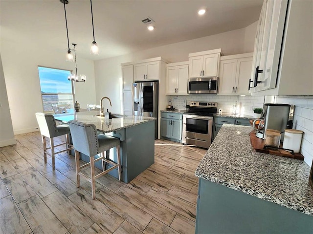 kitchen with appliances with stainless steel finishes, sink, pendant lighting, white cabinetry, and an island with sink