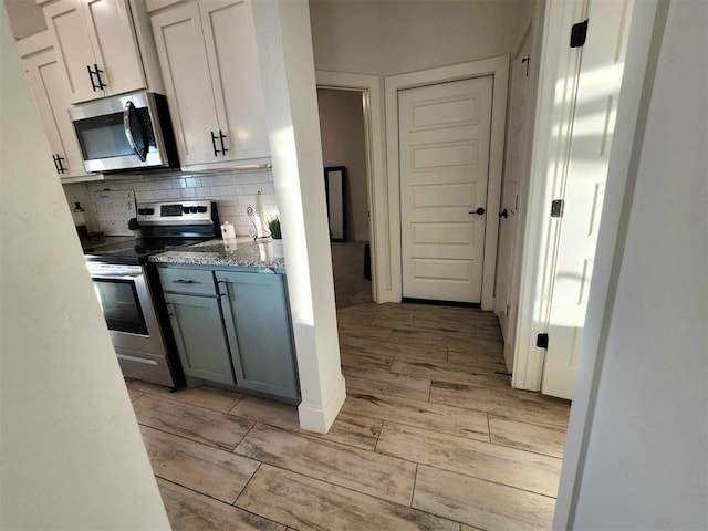 kitchen with decorative backsplash, stainless steel appliances, white cabinetry, and light hardwood / wood-style floors