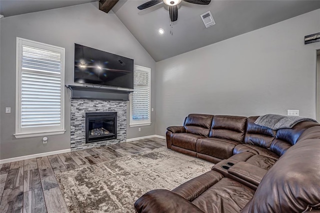 living room with ceiling fan, a wealth of natural light, a stone fireplace, vaulted ceiling with beams, and wood-type flooring