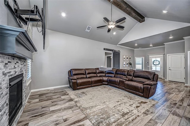 living room with lofted ceiling with beams, a stone fireplace, crown molding, ceiling fan, and a barn door