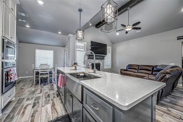 kitchen featuring white cabinetry, vaulted ceiling with beams, decorative light fixtures, a kitchen island with sink, and appliances with stainless steel finishes