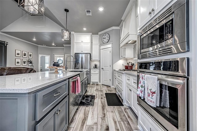 kitchen with backsplash, stainless steel appliances, a kitchen island with sink, white cabinets, and hanging light fixtures