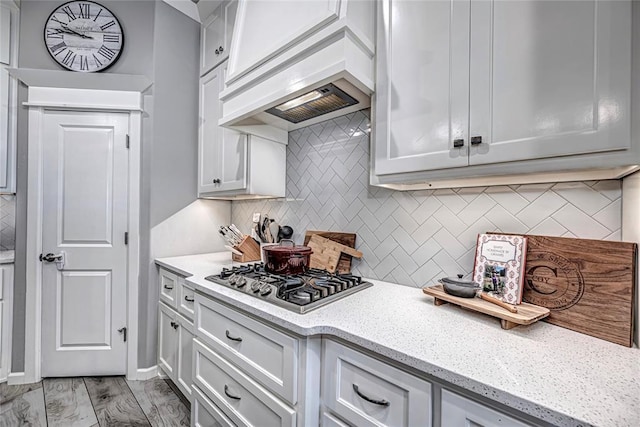 kitchen featuring light stone countertops, stainless steel gas cooktop, decorative backsplash, custom range hood, and light wood-type flooring