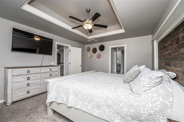 carpeted bedroom featuring a raised ceiling, ensuite bathroom, and ceiling fan