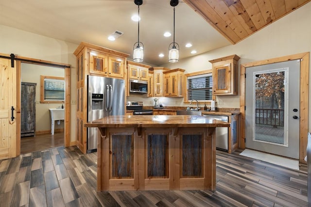 kitchen with appliances with stainless steel finishes, pendant lighting, a barn door, a center island, and butcher block counters