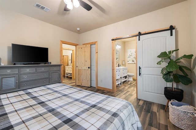 bedroom featuring a barn door, ensuite bathroom, ceiling fan, and hardwood / wood-style flooring