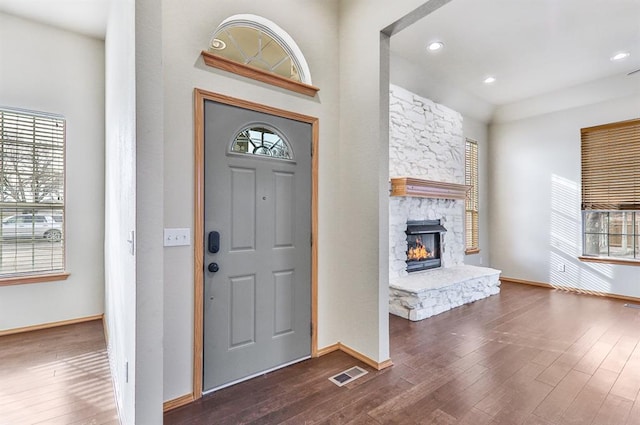 entrance foyer with baseboards, visible vents, dark wood-type flooring, a stone fireplace, and recessed lighting