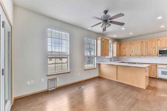 kitchen featuring light brown cabinets, oven, visible vents, tasteful backsplash, and stainless steel microwave