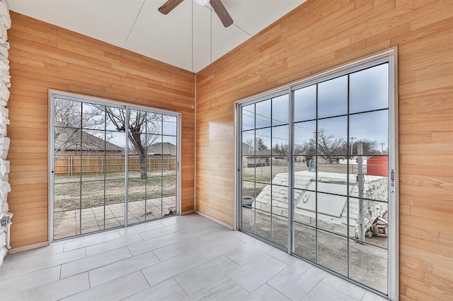 interior space with a ceiling fan, wood walls, and tile patterned floors