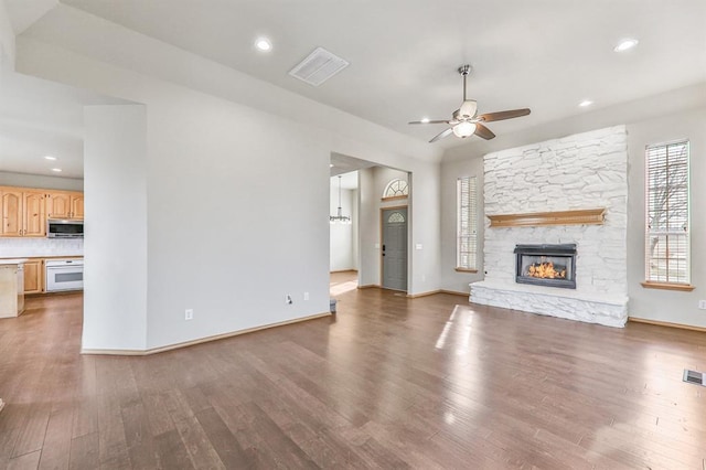 unfurnished living room with a ceiling fan, visible vents, a stone fireplace, and wood finished floors