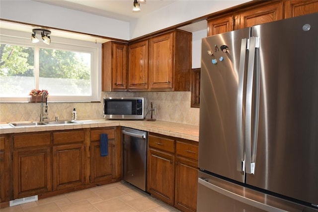 kitchen with appliances with stainless steel finishes, backsplash, sink, light tile patterned floors, and tile countertops