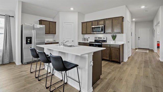 kitchen with dark brown cabinetry, stainless steel appliances, light hardwood / wood-style floors, a breakfast bar area, and an island with sink