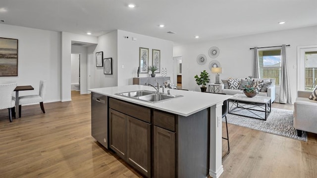 kitchen featuring light wood-type flooring, stainless steel dishwasher, dark brown cabinets, sink, and an island with sink