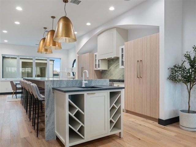 kitchen featuring sink, tasteful backsplash, light hardwood / wood-style flooring, an island with sink, and pendant lighting