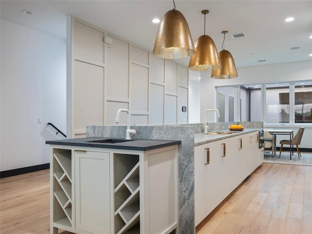 kitchen with pendant lighting, white cabinetry, sink, and a kitchen island with sink