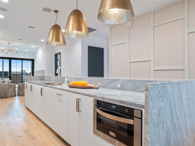 kitchen with stainless steel oven, white cabinets, sink, hanging light fixtures, and light stone counters