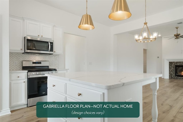 kitchen with a tile fireplace, white cabinets, light hardwood / wood-style flooring, a kitchen island, and appliances with stainless steel finishes