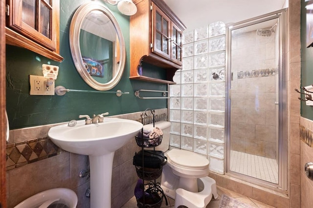 bathroom with tile patterned floors, toilet, tile walls, and a shower with shower door