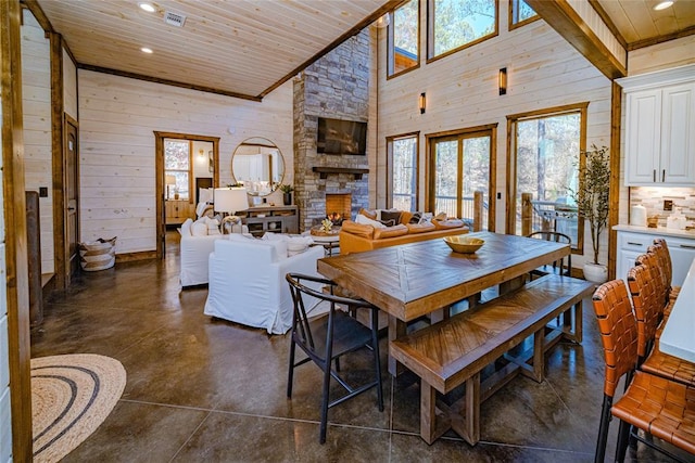 dining space with a stone fireplace, wooden walls, wood ceiling, and a high ceiling