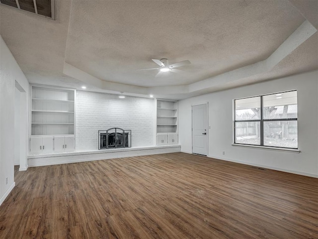 unfurnished living room featuring built in shelves, ceiling fan, hardwood / wood-style floors, a textured ceiling, and a tray ceiling