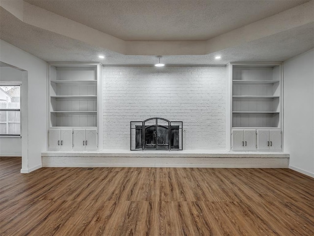 unfurnished living room featuring hardwood / wood-style flooring, built in features, a textured ceiling, and a brick fireplace