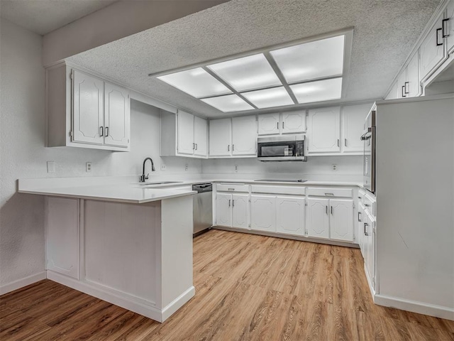 kitchen featuring kitchen peninsula, light wood-type flooring, stainless steel appliances, sink, and white cabinets